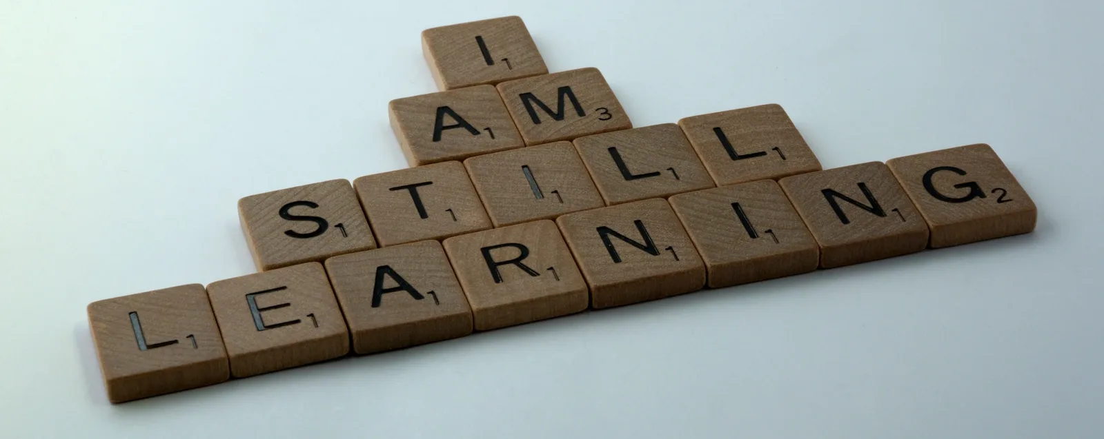 Brown wooden blocks with letters on them, arranged to spell, "I am still learning"