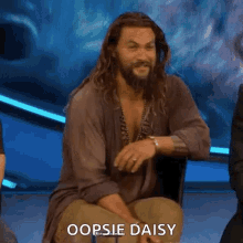Jason Momoa posing adorably with the words "Oopsie Daisy" displayed.