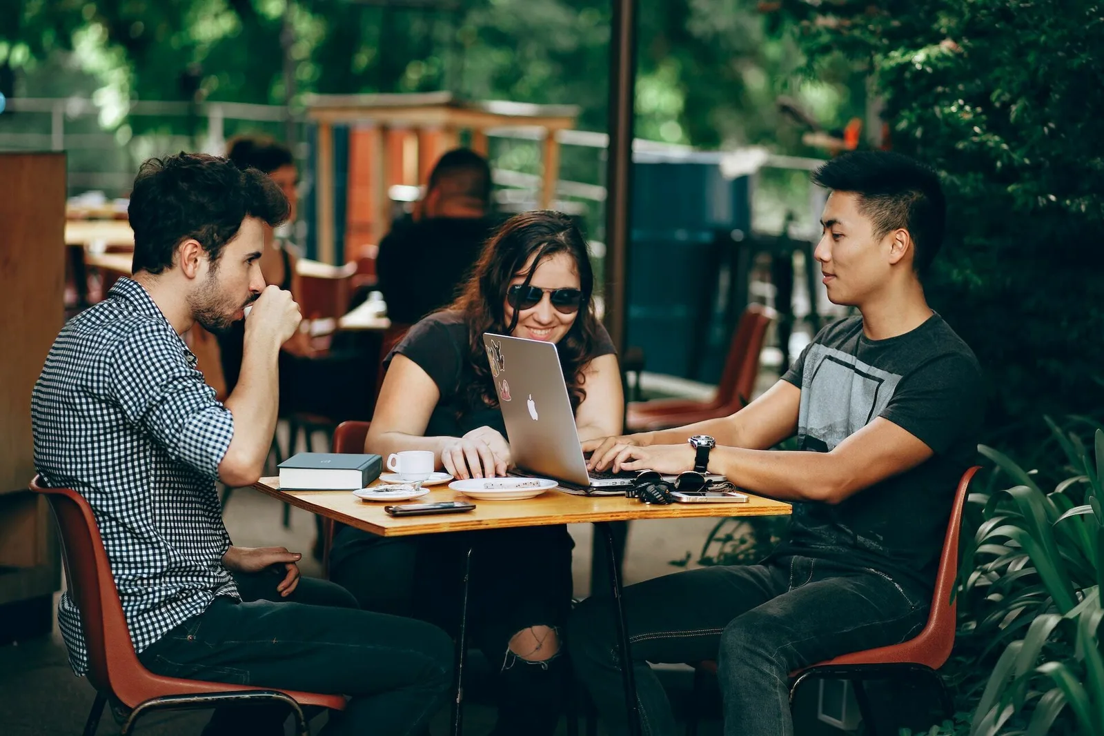 Three people sitting at a coffee shop working on their computers and smiling.
