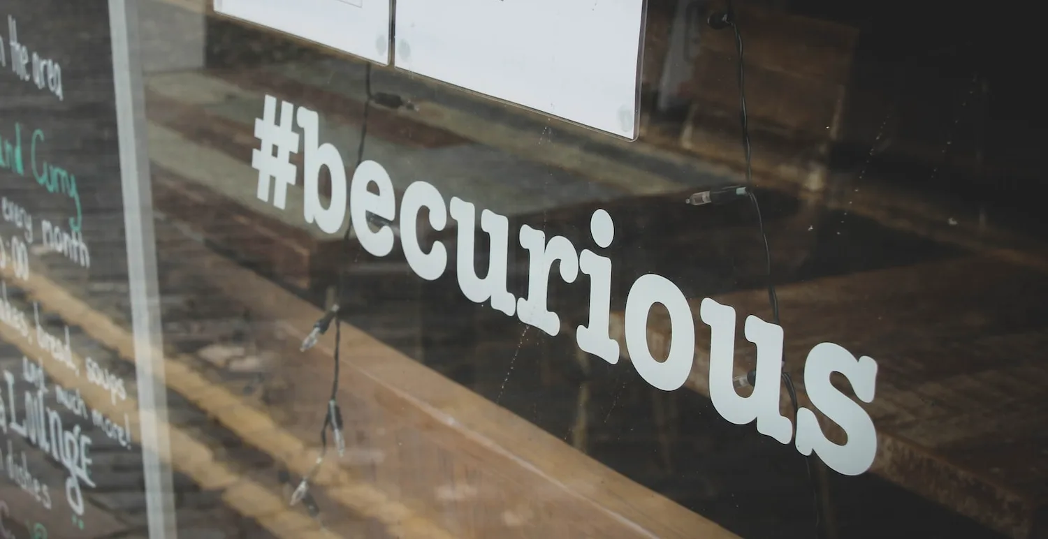 A sign on a window that says "#becurious"
